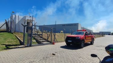 Bomberos trabaja en un incendio de campo que rodea depósito de empresa de vestimenta