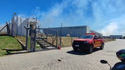 Bomberos trabaja en un incendio de campo que rodea depósito de empresa de vestimenta